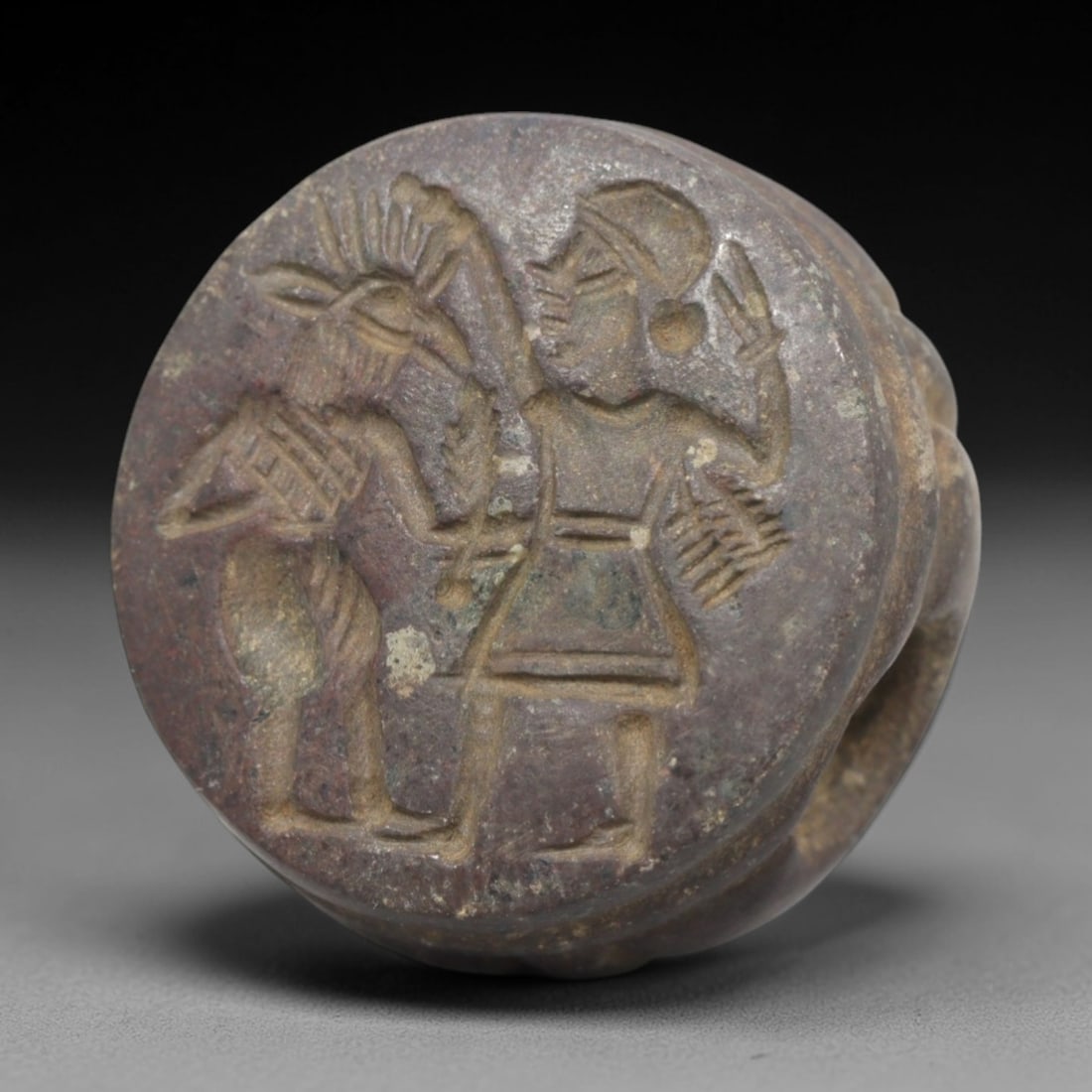 Ancient Stone Hemispherical Stamp Seal - Near Eastern Figural Scene, 36ZP: Crafted from a dense, reddish-brown stone, this hemispherical stamp seal bears a deeply incised narrative scene featuring two stylized figures: a horned anthropomorphic deity with a spiked headdress a