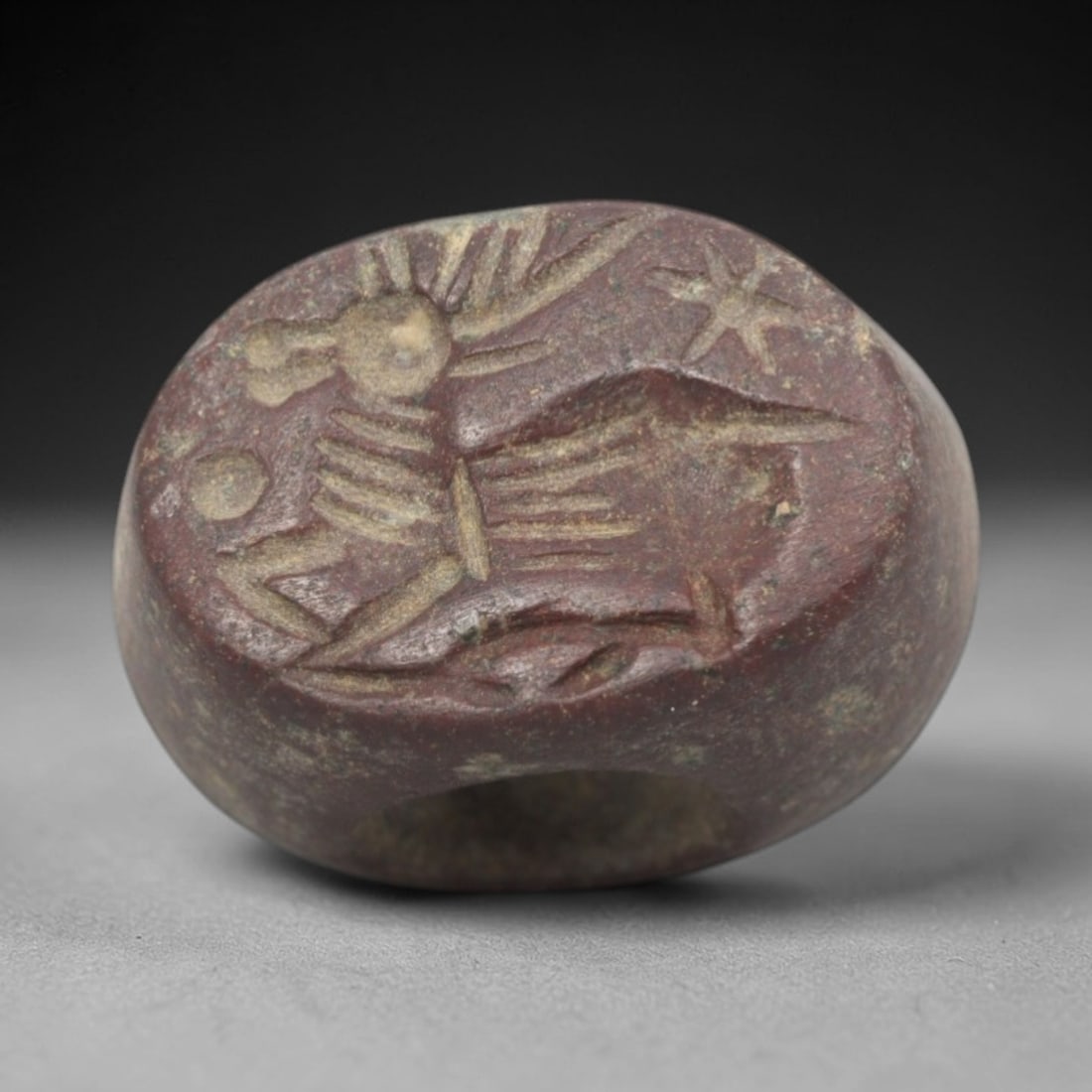 Ancient Stone Hemispherical Stamp Seal - Near Eastern Ibex Star Figure, 60ZS: Crafted from dense, reddish-brown stone, this hemispherical stamp seal bears incised carving of a leaping ibex, with prominent curved horns, segmented torso, and dynamic linear limb motifs, alongside