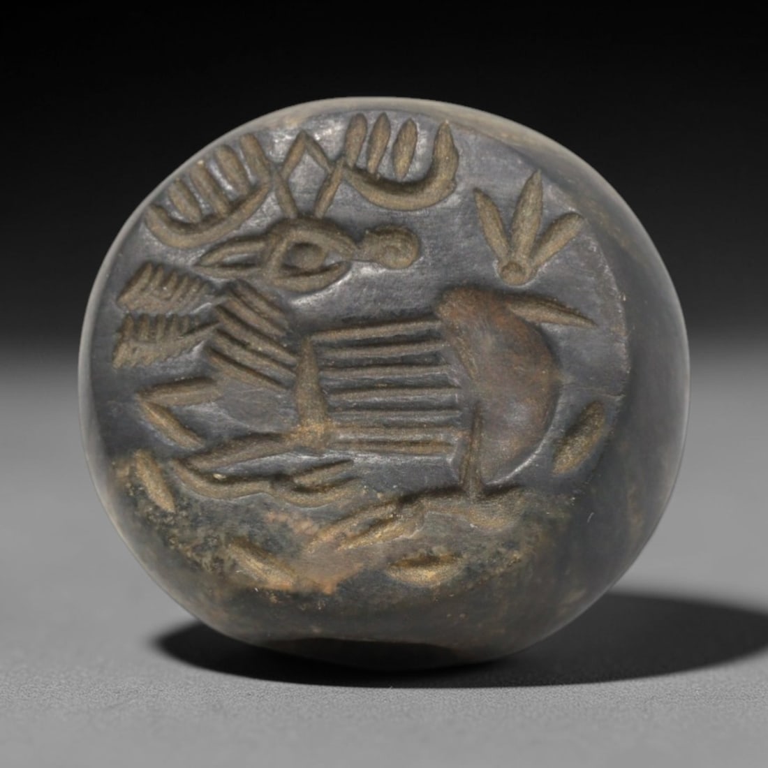 Ancient Stone Hemispherical Stamp Seal - Near Eastern Ibex Scene, 31ZP: Crafted from a dense, dark stone with subtle golden patina, this hemispherical stamp seal bears a deeply incised depiction of a stylized ibex, rendered in linear relief with distinct segmented body, c