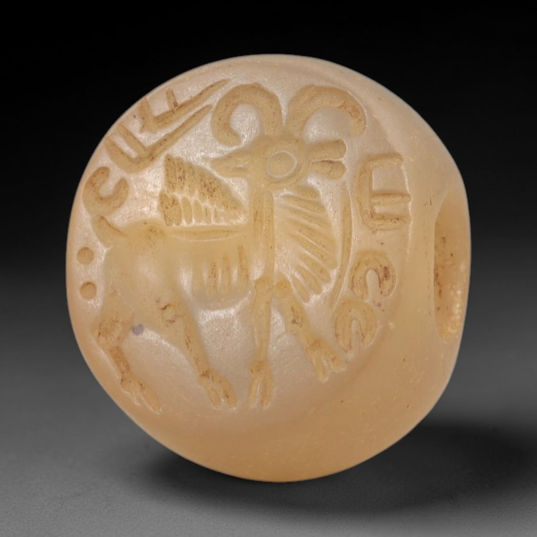 Ancient Chalcedony Stamp Seal - Sasanian Winged Ram, 65AK: Carved from translucent chalcedony, this spherical Sasanian stamp seal features a central winged ram motif with curved horns, feathered wings, and ribbed body, encircled by incised epigraphic script a