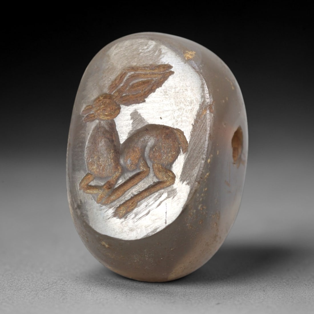 Ancient Stone Hemispherical Stamp Seal - Near Eastern Hare Figure, 43ZS: Crafted from translucent, light grayish stone (likely chalcedony), this hemispherical stamp seal bears incised carving of a crouching hare, with large, stylized ears, compact body detailing, and linea