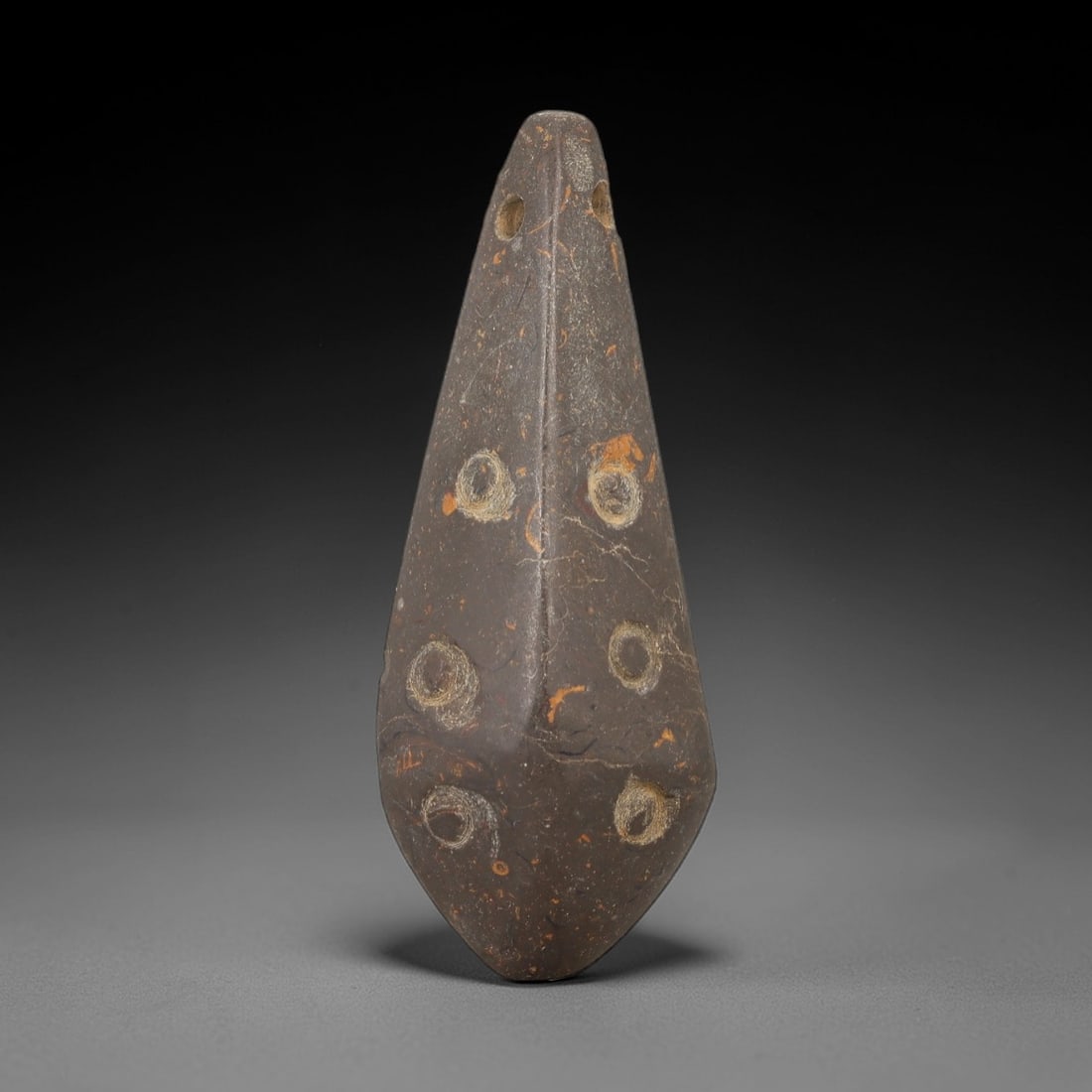 Ancient Stone Eye Amulet - Near Eastern Pendant, 40AE: This artifact is a carved stone eye amulet of Near Eastern origin, crafted from a dark brown stone with natural orange mineral inclusions and fine surface veining. Its elongated, teardrop-shaped form