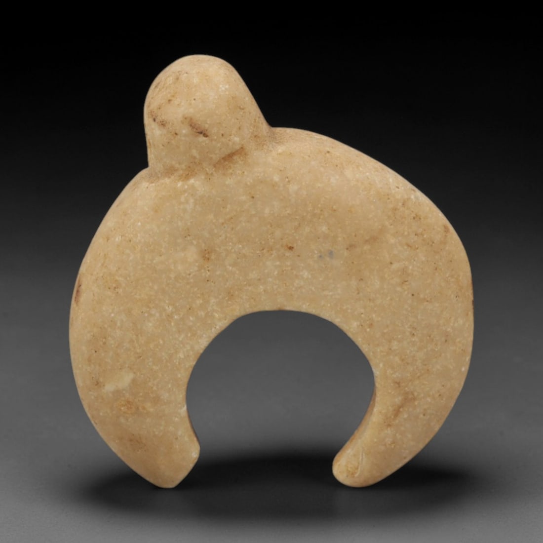 Ancient Stone Crescent Amulet - Near Eastern Pendant, 89XQ: Carved from a pale beige stone, this amulet takes a distinct crescent form with a perforated tab at the apex for suspension, its surface smooth and weathered with subtle mineral inclusions. The cresce