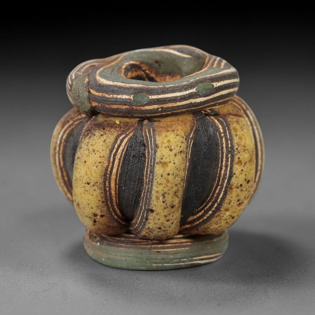 Ancient Glass Bead - Islamic Trailed Bead, 38ZM: This ancient bead is crafted from polychrome glass, formed using the trailed decorative technique characteristic of Islamic glassworking traditions. The lobed, multi-segmented form features alternatin