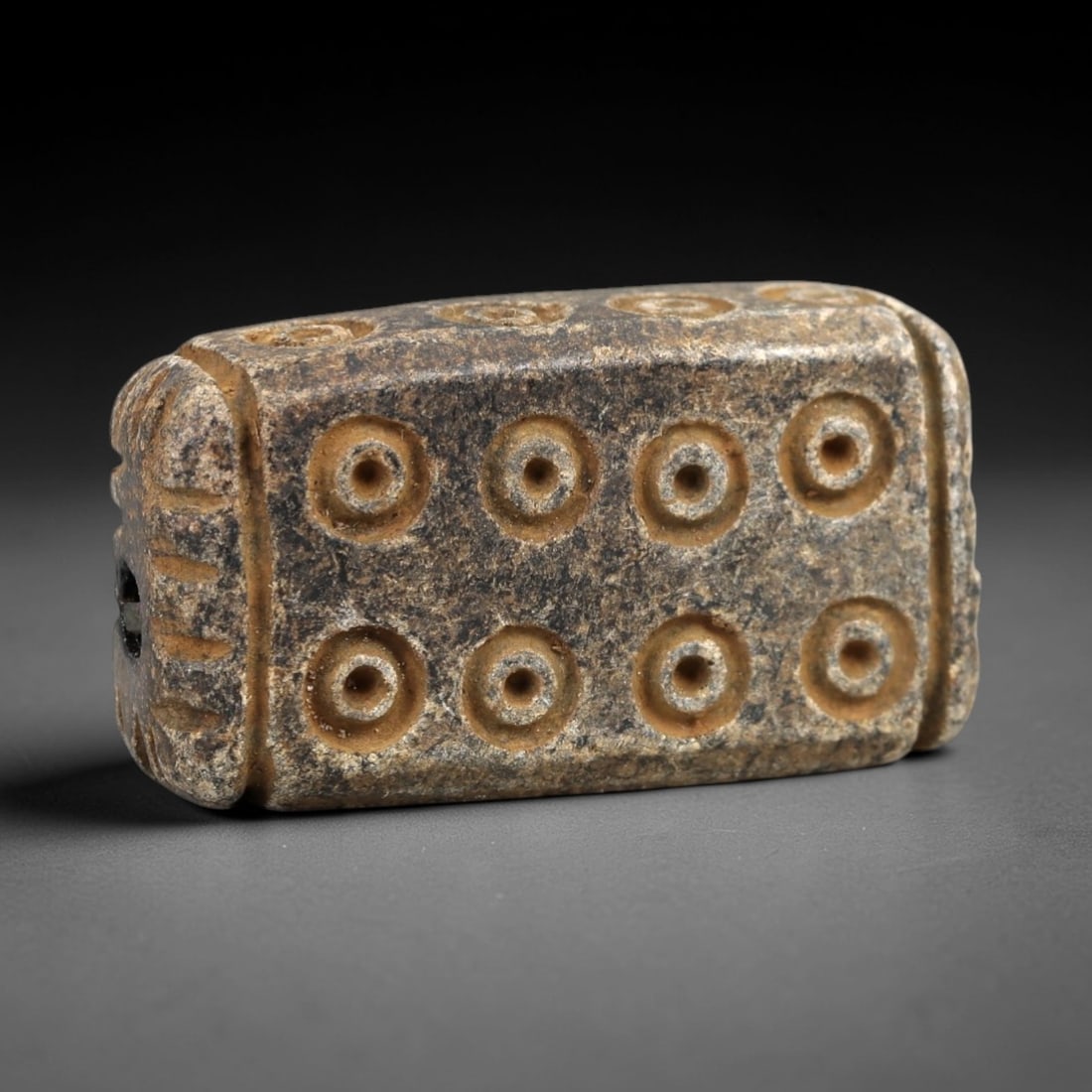 Ancient Steatite Amulet - Near Eastern Concentric Circles, 35AK: Crafted from steatite, this rectangular prism amulet features incised concentric circle motifs arranged in a 2x4 grid across its primary face, with decorative linear carvings framing the suspension ho