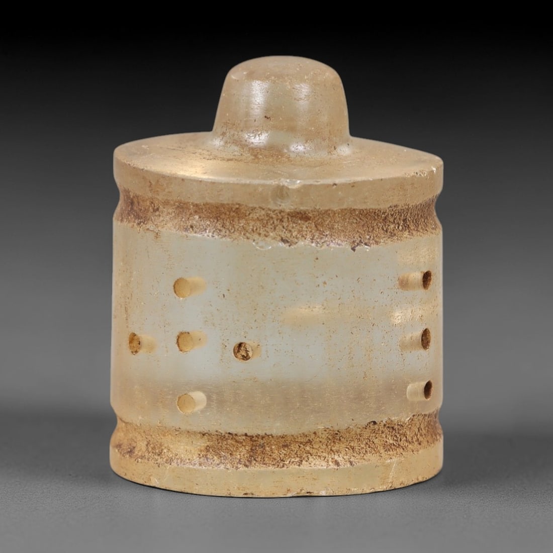 Ancient Glass Medieval Relic - Near Eastern Artifact, 63AL: This artifact is crafted from ancient glass, formed into a cylindrical shape with a raised, rounded knob at the top and a distinct, thickened base. The body of the relic features a series of small, dr