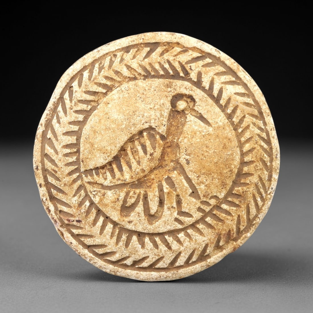 Ancient Stone Double Convex Bead - Near Eastern Animal Motif, 81AL: Carved from pale tan limestone, this double convex bead relic features two distinct circular impression faces, each bordered by a chevron-patterned incised border. One face depicts a stylized wading b