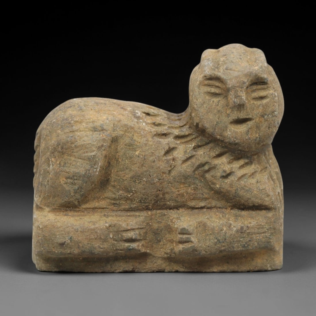 Ancient Stone Human-Headed Lion Effigy - Near Eastern Figurine, 92ZP: This artifact is a carved stone human-headed lion effigy, executed in the hybrid zoomorphic tradition of the ancient Near East. The effigy depicts a recumbent lion with a stylized human face-closed ey
