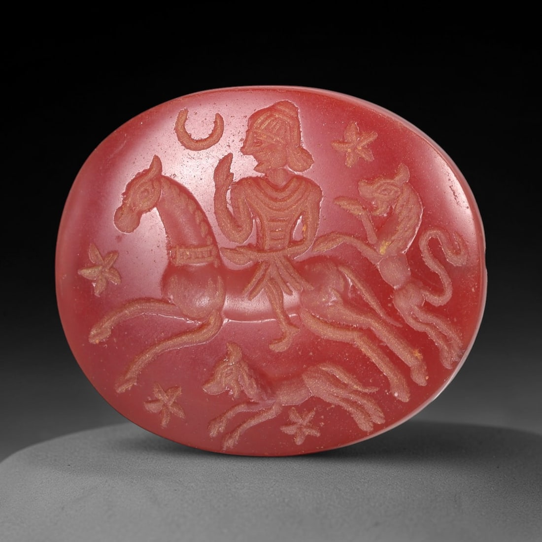 Ancient Carnelian Amulet - Near Eastern Intaglio Relic, 15AM: This intaglio bead is carved from carnelian, a material prized in ancient Near Eastern art for its vivid hue and symbolic significance. The carving depicts a central figure on horseback, flanked by an