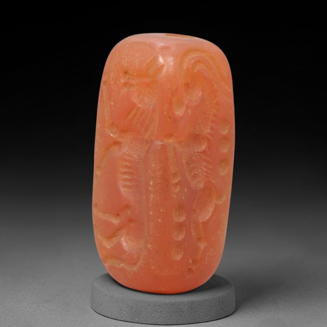 Ancient Carnelian Cylinder Seal - Near Eastern Amulet, 19XV: Carved from warm orange-red carnelian, this cylinder seal features incised figural and decorative motifs across its cylindrical surface, including stylized animal forms and linear dot patterns charact