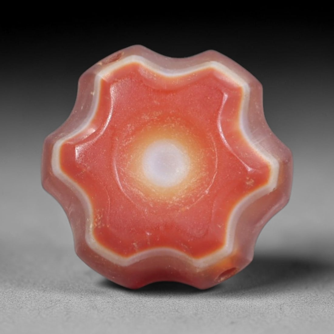 Antique Agate Star Bead - Central Asian Carved Gemstone, 2AR: Carved from banded agate with a rich red-orange base and creamy white concentric banding, this bead features a scalloped eight-pointed star form with a central circular eye motif. Two lateral perforat