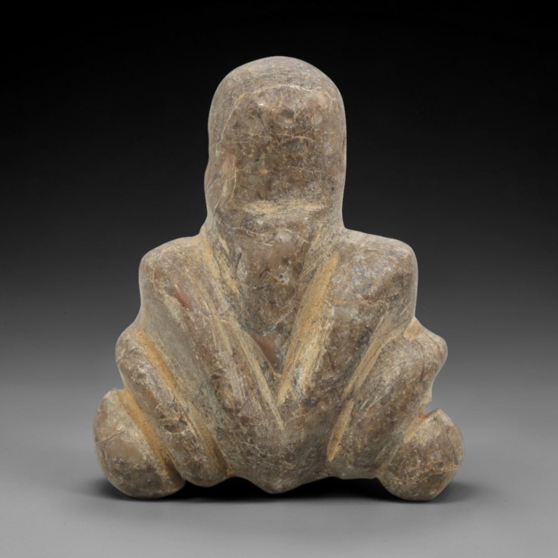 Ancient Near Eastern Stone Anthropomorphic Amulet - Carved Figurine, 94ZW: This amulet is carved from a mottled, greyish-brown stone, likely a type of siltstone or conglomerate, with incised linear details defining its stylized seated anthropomorphic form. The piece features