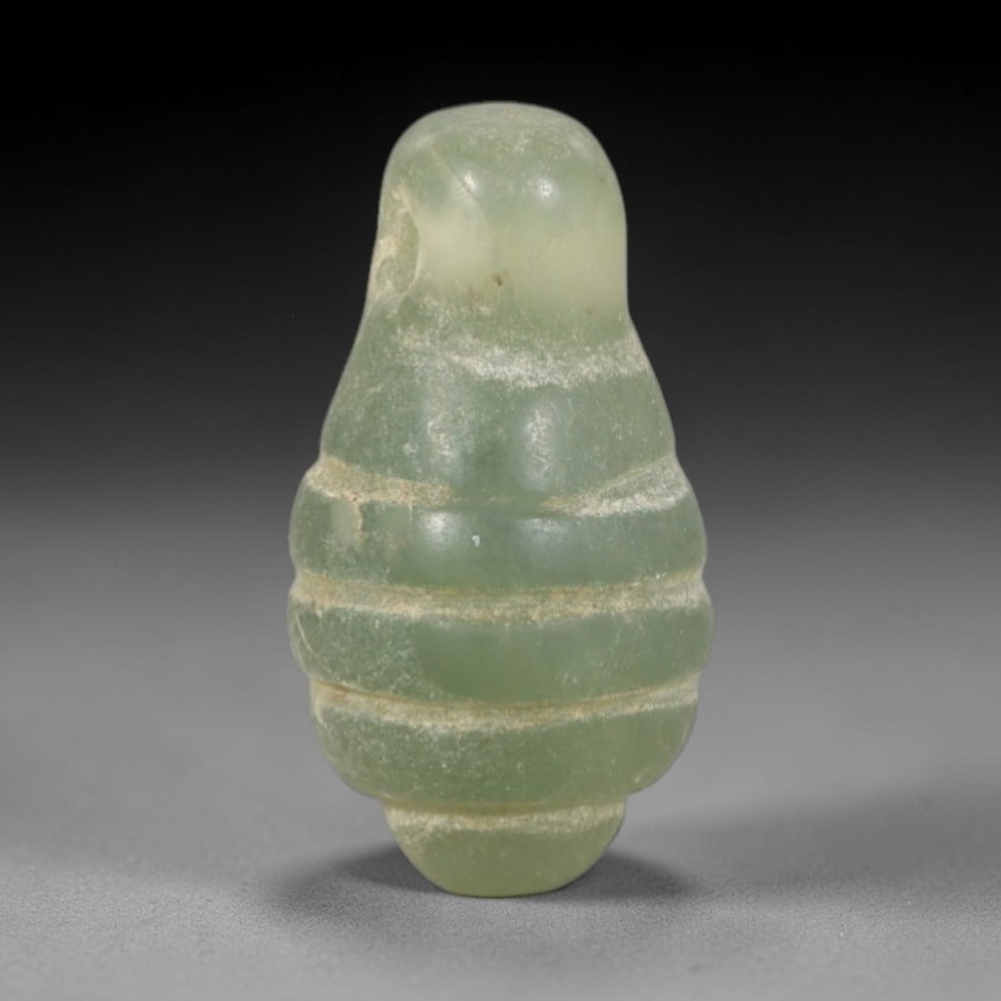 Ancient Green Stone Amulet - Egyptian Carved Pendant, 43AR: This artifact is carved from a pale, translucent green stone with a smooth, polished surface and subtle natural inclusions consistent with age. The form is a compact, segmented amulet with horizontal