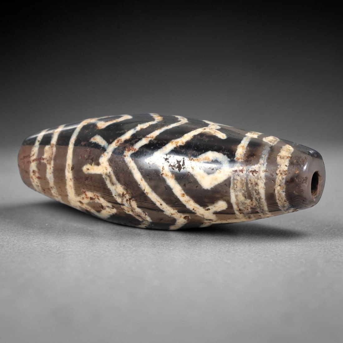 Ancient Agate Dzi Bead - Himalayan Etched Amulet, 9AS: This ancient elongated bead is fashioned from banded agate, showcasing a dark brown base with intricate white etched geometric motifs, including chevron and linear patterns that define the classic Him