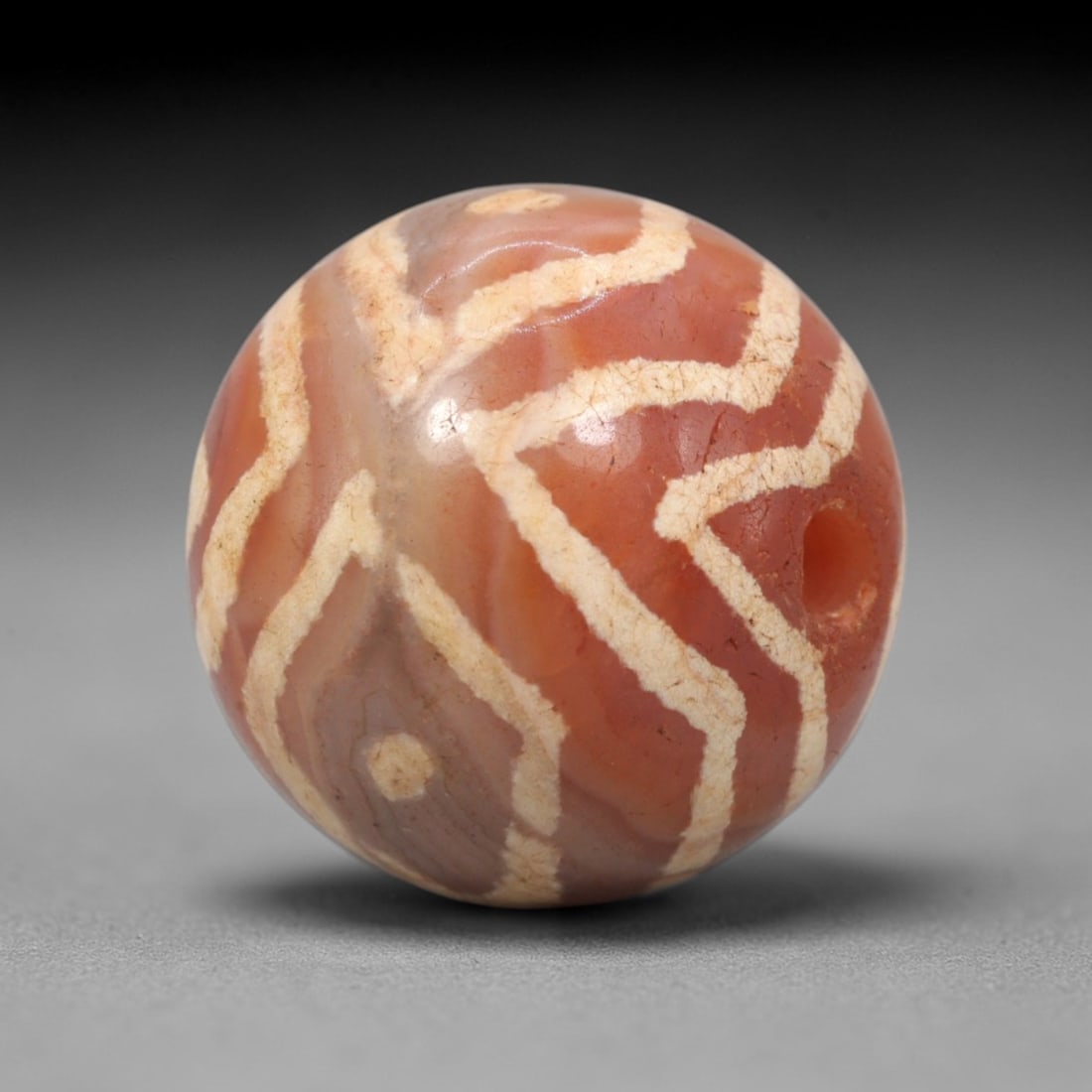 Ancient Carnelian Wavy Geometric Dzi Bead - Himalayan Amulet, 70XV: Crafted from warm banded carnelian, this spherical bead features continuous etched white wavy geometric lines and small circular dot accents, executed in traditional Himalayan Dzi bead techniques. The