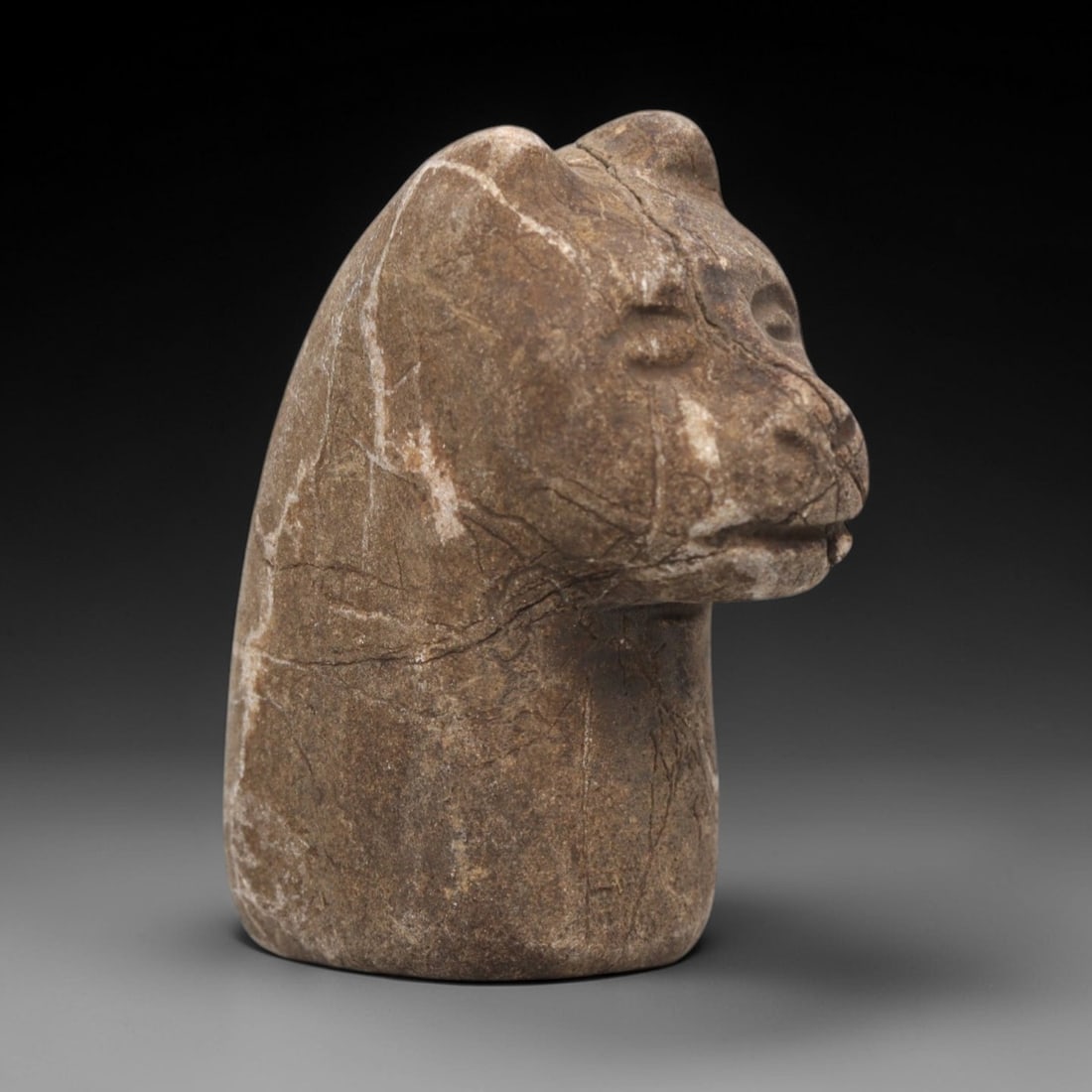 Ancient Stone Zoomorphic Head - Near Eastern Animal Carving, 63ZV: This artifact is a carved stone zoomorphic head, crafted from a granular, earth-toned stone consistent with ancient Near Eastern lithic traditions. The relief carving depicts a stylized animal head, l