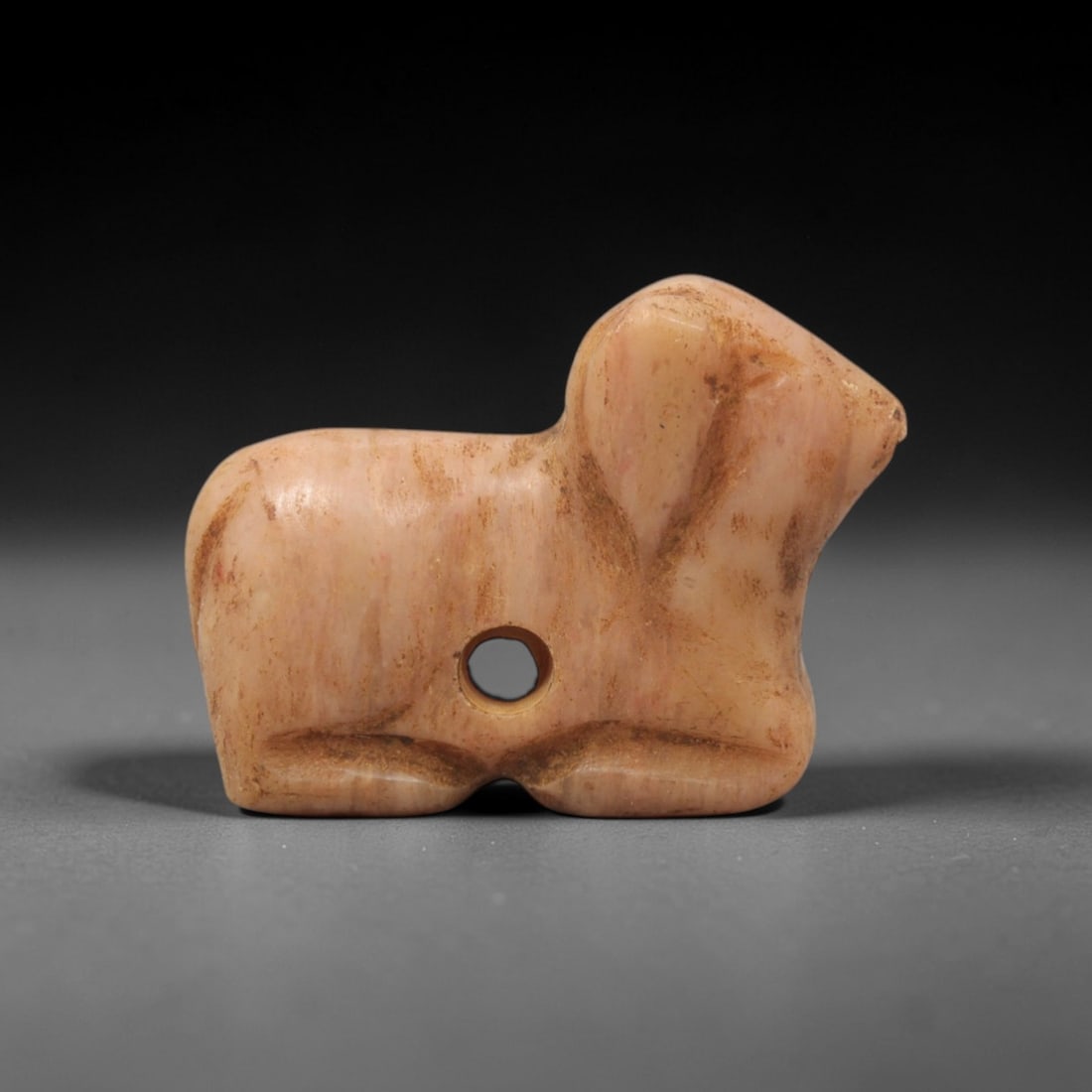 Ancient Stone Ram Amulet - Near Eastern Figurine, 9XT: This amulet is carved from pink-hued stone with subtle brown veining throughout the form, crafted using a straightforward yet intentional carving technique that defines the recumbent ram's silhouette.