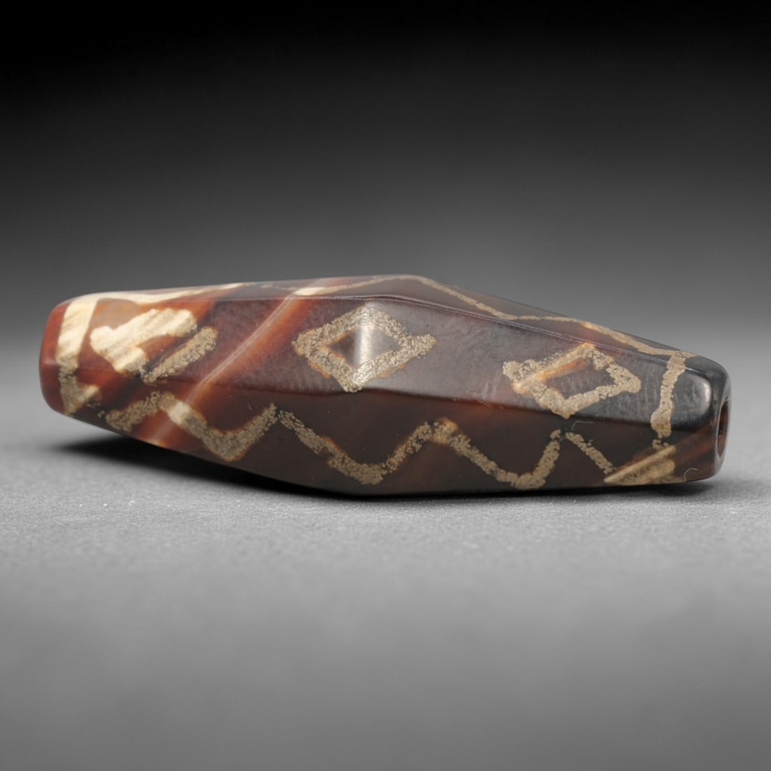 Ancient Agate Etched Dzi Bead - Himalayan Amulet, 85XV: Crafted from banded agate, this faceted bead features etched geometric motifs including wavy lines and diamond shapes, executed in traditional Himalayan Dzi bead techniques. The form is an elongated,