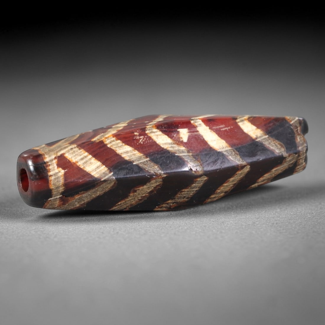 Ancient Agate Dzi Bead - Himalayan Chevron Pendant, 1AS: This ancient etched bead is crafted from polished agate, featuring a rich carnelian-hued base with contrasting white etched chevron motifs. The bead exhibits the characteristic elongated, multi-facete