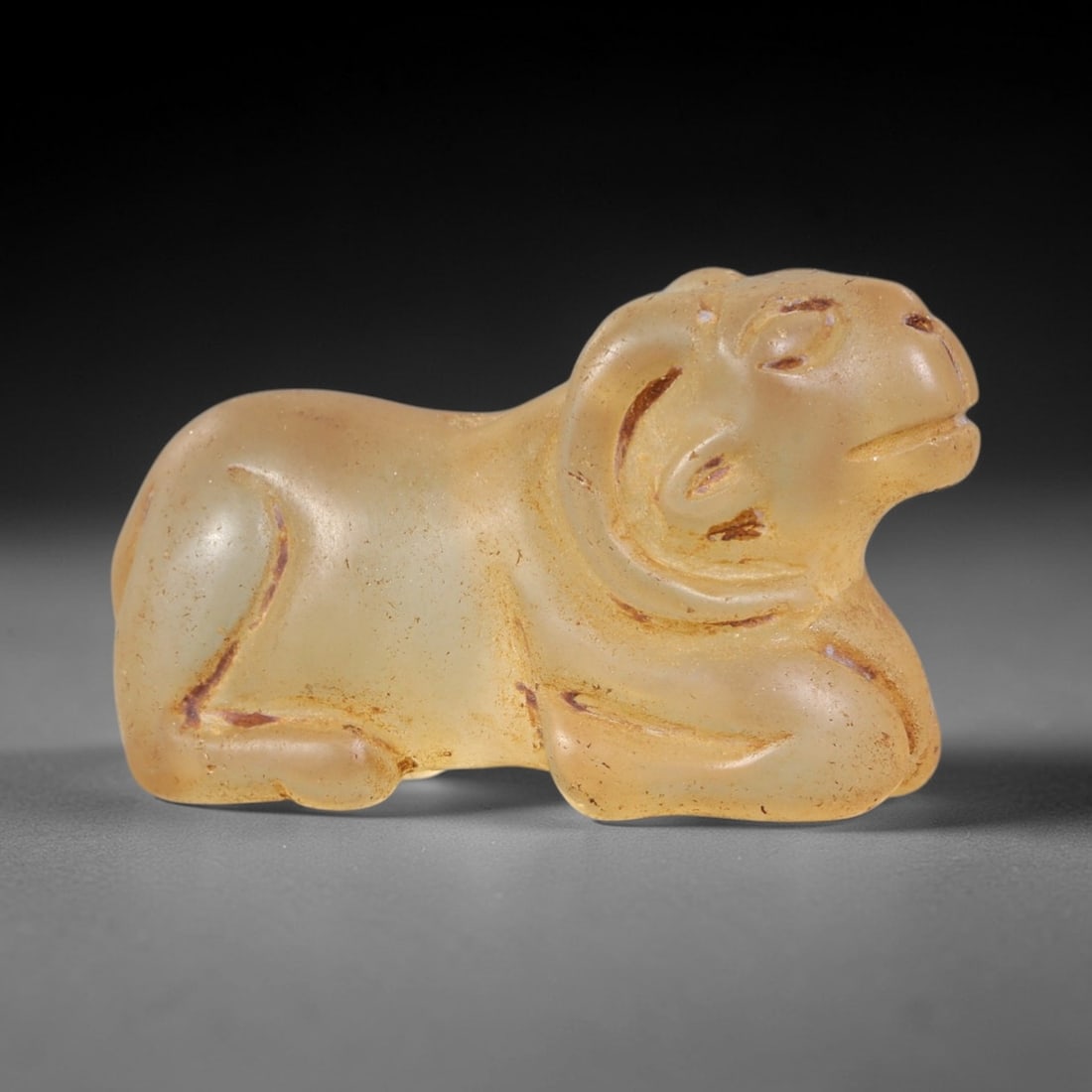 Ancient Glass Ram - Near Eastern Zoomorphic Amulet, 17AS: This zoomorphic amulet is carved from translucent pale yellow glass, exhibiting a smooth, luminous surface with subtle amber patination and fine incised details consistent with ancient Near Eastern ar