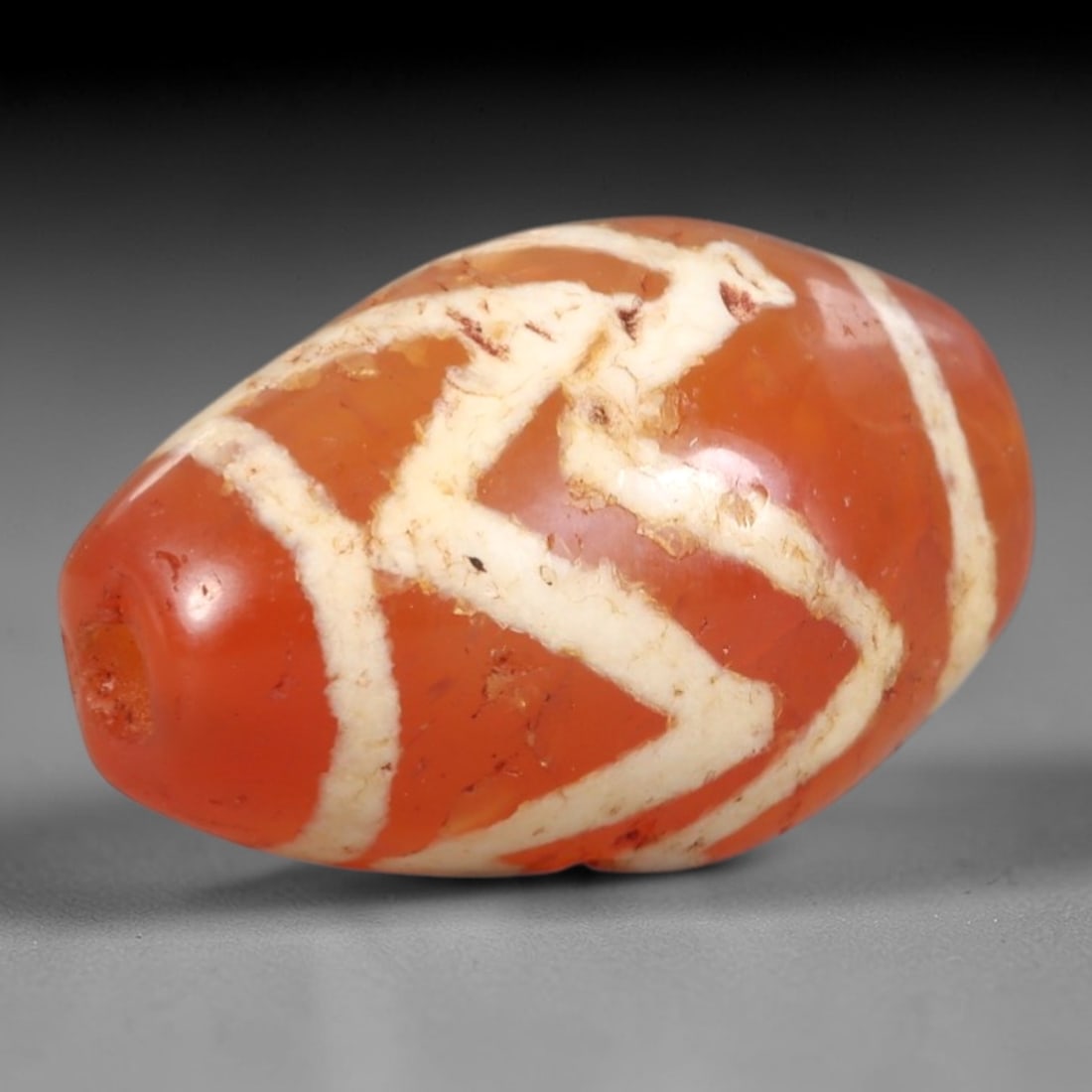 Ancient Carnelian Etched Dzi Bead - Himalayan Amulet, 100AR: Crafted from translucent carnelian, this bead features intricate etched white patterns, including stylized 'V' motifs and linear bands, applied using traditional Himalayan techniques. The form is an e