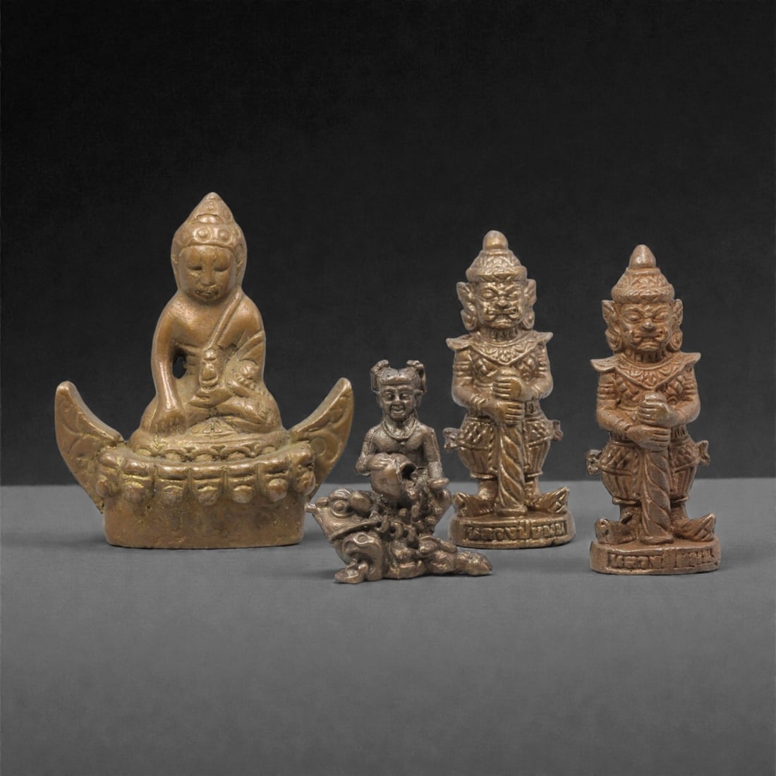 Four Thai Bronze Buddhist and Guardian Miniature Figures, 20th Century, 20FM: Cast from bronze with a warm patina, the set comprises four miniature devotional figures: a seated Buddha on a boat-shaped base, a figure seated atop a mythical beast, and two guardian figures with fi
