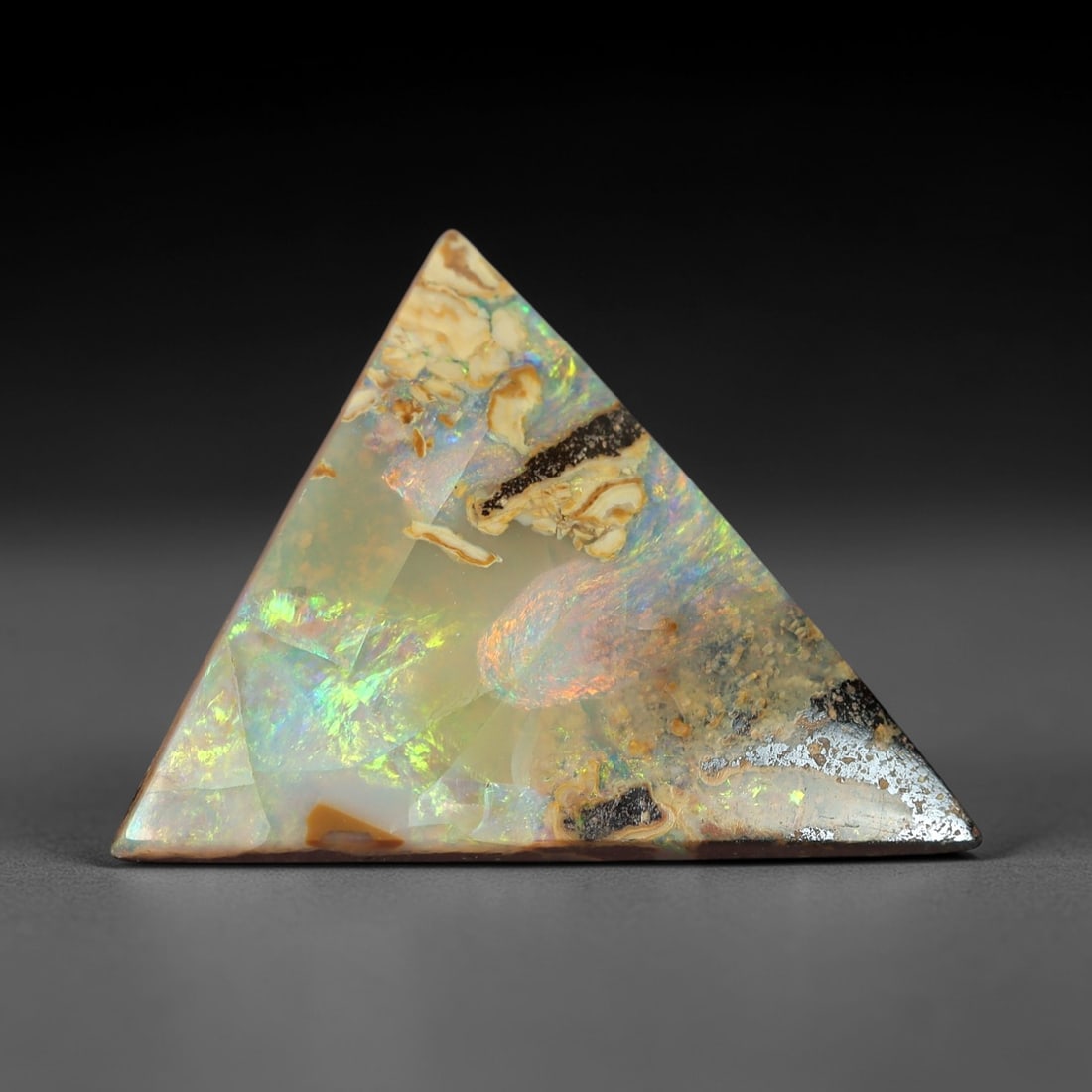 5.07 Carats Iridescent Multicolor Boulder Opal - Natural Australian Stone, 56XM: This striking boulder opal dazzles with a kaleidoscopic play of color, shifting through vivid greens, pinks, and iridescent blues across its triangular cabochon form. The stone's translucent, milky ba