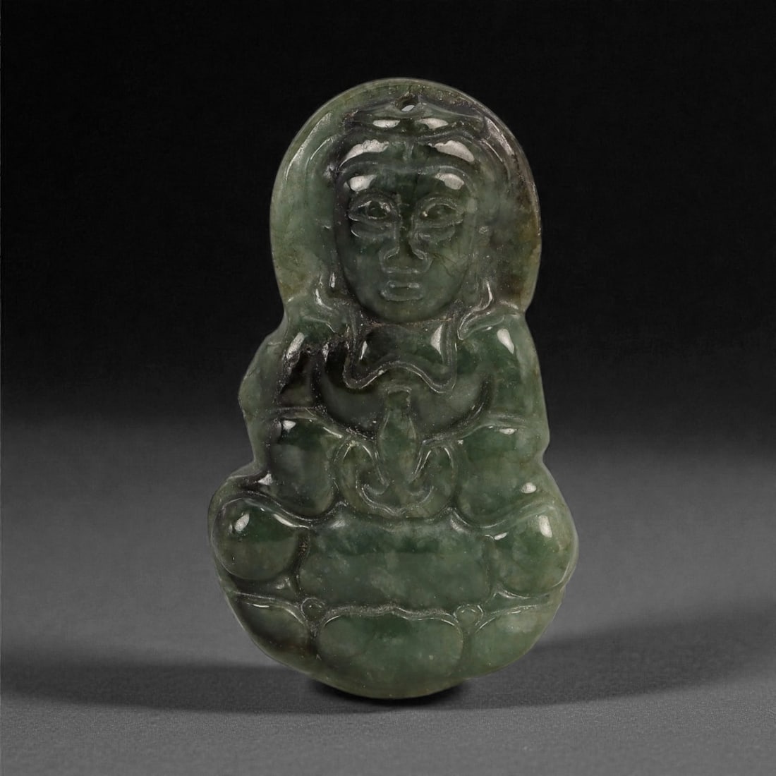 A Chinese Jadeite Jade Buddha Amulet Pendant, 20th Century, 46YB: Carved from mottled dark green jadeite with lighter translucent inclusions and natural clouding, the pendant is worked in relief to depict a seated Buddha deity shown frontally, with a rounded head fr