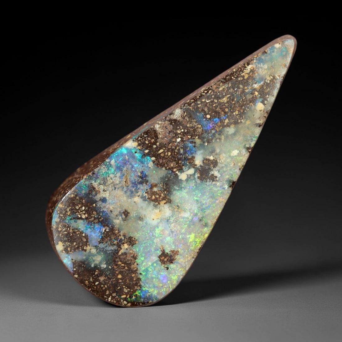 7.13 Carats Multicolor Iridescent Boulder Opal Cabochon - Natural Australian Stone, 50XM: This striking boulder opal cabochon features an elongated, tapered form with a rich brown ironstone matrix interspersed with vibrant, iridescent opal inclusions. The stone's polished surface showcases