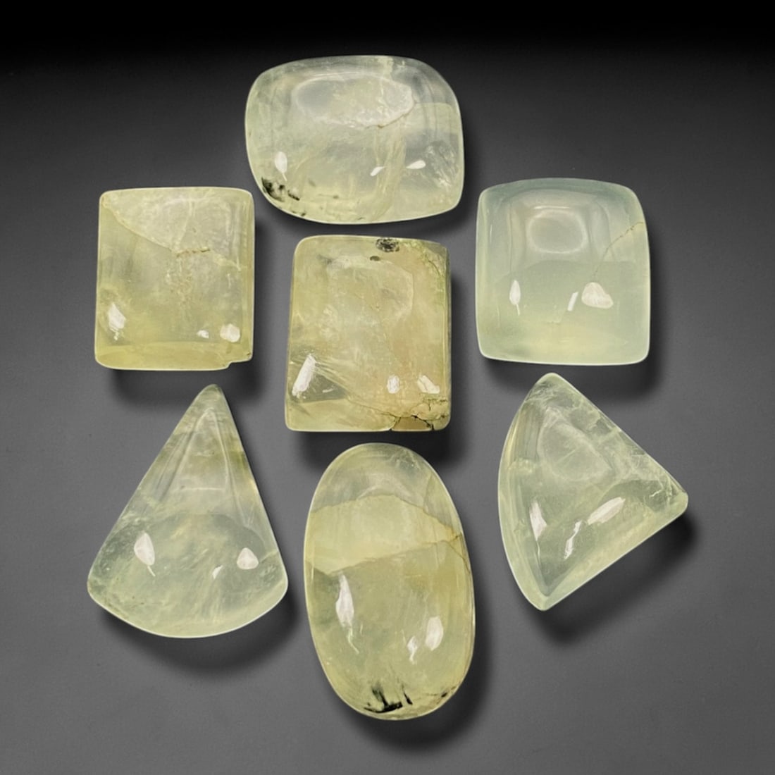 165.24 Carats Pale Green Prehnite Cabochon Parcel - Natural Malagasy Stones - 1.6-2.3cm, 65ZJ: This curated parcel of loose prehnite cabochons captivates with a soft, translucent pale green hue, each stone radiating a gentle, milky glow that evokes the quiet beauty of a forest stream. The inter