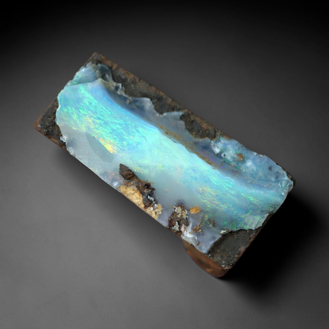 11.79 Carats Winton Boulder Opal Rough - Broad Blue-Green Play-of-Color Specimen, 33XM: This 11.79ct Winton boulder opal rough, measuring 18x9mm, is a striking example of Australia's iconic gemstone, showcasing the raw beauty of nature's artistry. The specimen retains its natural ironsto