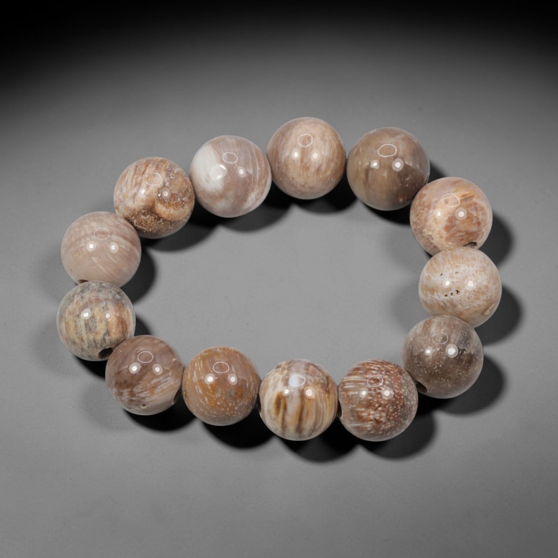 A Chinese Fossilised Wood Bead Bracelet, 20th Century, 80FS: Composed of spherical beads of fossilised wood with natural banding and minor internal inclusions, the bracelet is strung in a continuous loop. The beads exhibit a smooth, polished surface with subtle