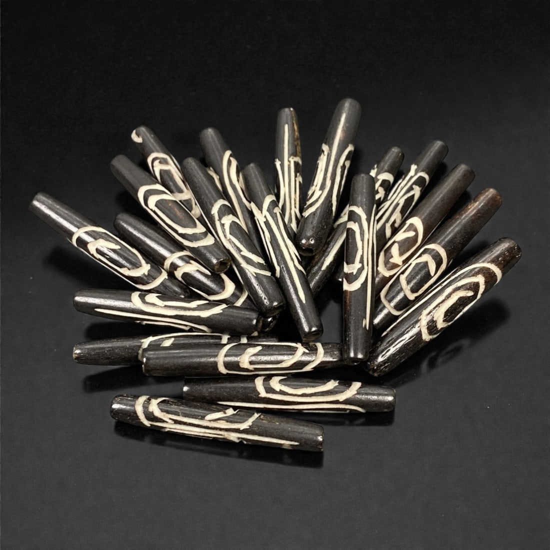 A Lot of Tibetan Bone Beads with Scroll Inlay Motif, 20th Century, 70S: A substantial grouping of elongated, tubular bone beads, characteristic of Tibetan Buddhist devotional art. Each bead is uniformly shaped with a slender, tapered form and features the iconic scroll in