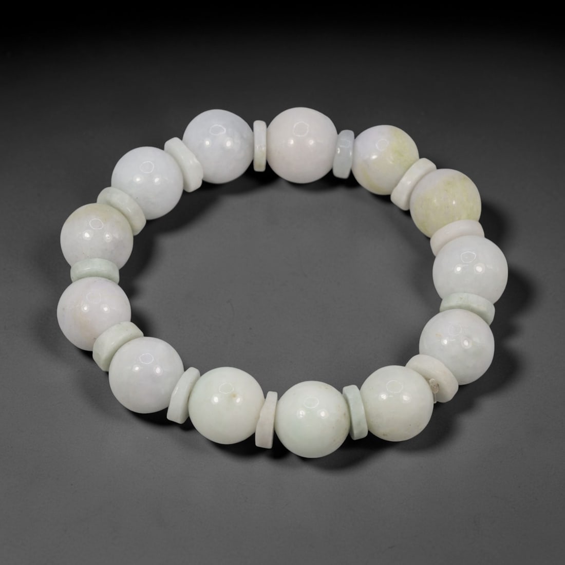 A Chinese Jadeite Jade Bead Bracelet, 20th Century, 78FS: Composed of spherical beads of pale white and celadon jadeite jade with natural veining and minor internal inclusions, the bracelet is strung in a continuous loop. The beads exhibit a smooth, polished
