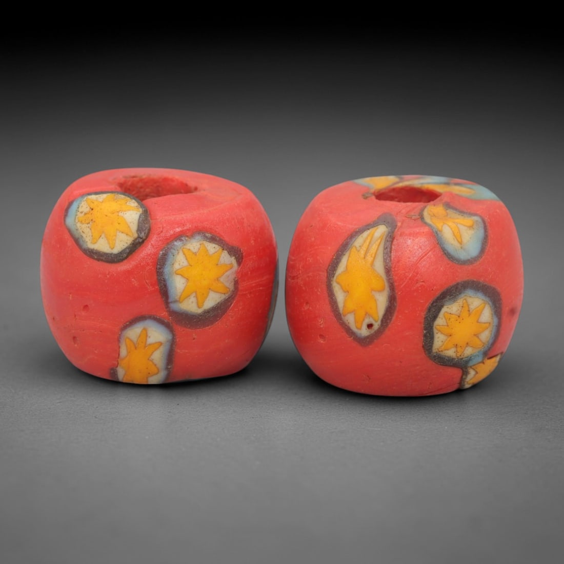 A Pair of Venetian Millefiori Glass Beads, 19th-20th Century, 45AD: Fabricated from opaque red glass, each bead is formed as a short cylinder with a central drilled perforation. The surface is decorated with characteristic millefiori canes, featuring star-shaped motif