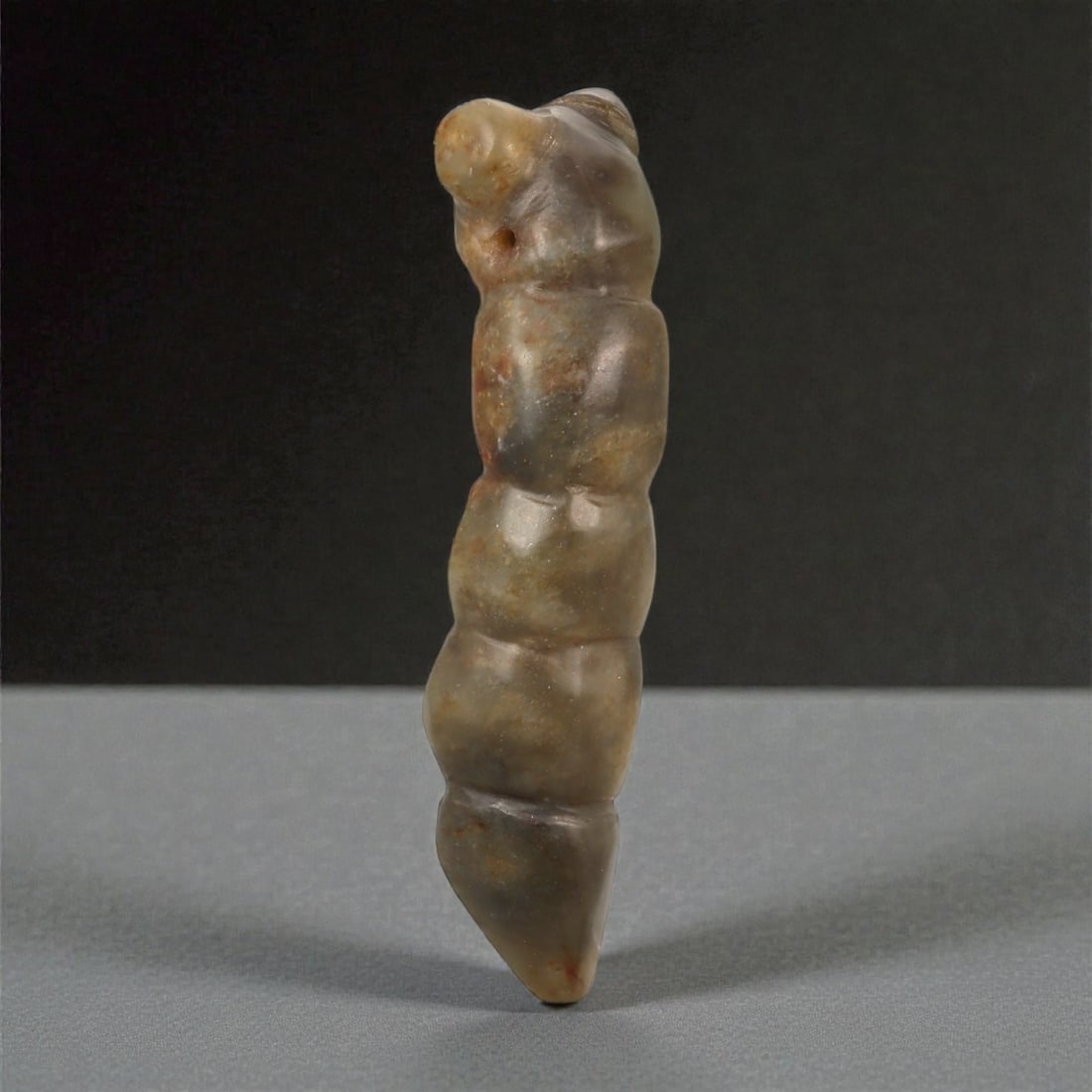 A Chinese Jade Worm Carving, Qing Dynasty, 18th-19th Century, 64FB: Carved from mottled jade with grey-green tones and areas of brownish mineral inclusions, the object is modeled in the round as a stylized worm or larval form. The body is elongated and vertically orie