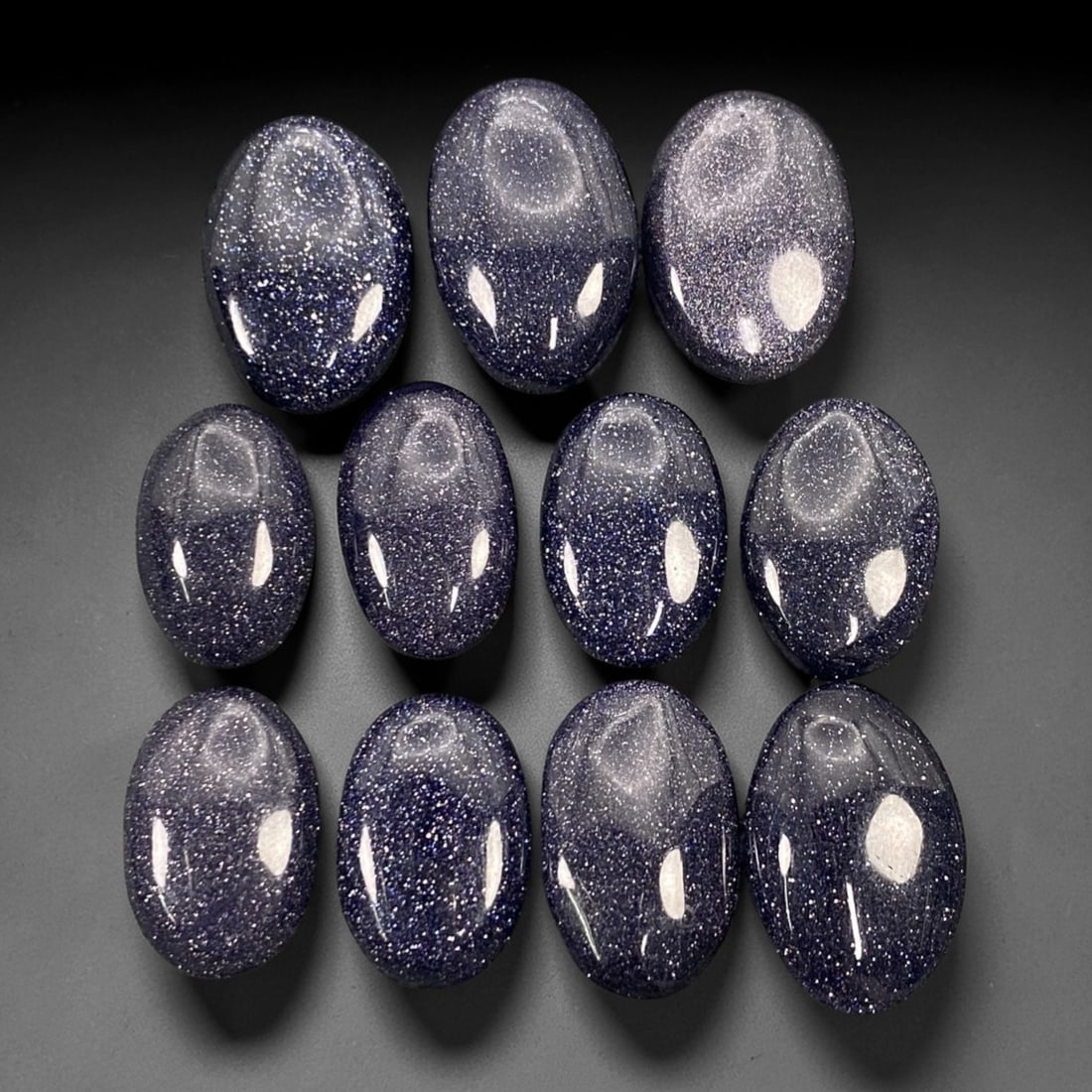 109.08 Carats Midnight Blue Goldstone Cabochon Parcel 1.7-2cm, 74ZJ: This luminous parcel of midnight blue goldstone cabochons shimmers with a celestial sparkle, evoking the quiet magic of a starry night sky. Each oval cabochon, sized between 1.7 and 2 centimeters, glo