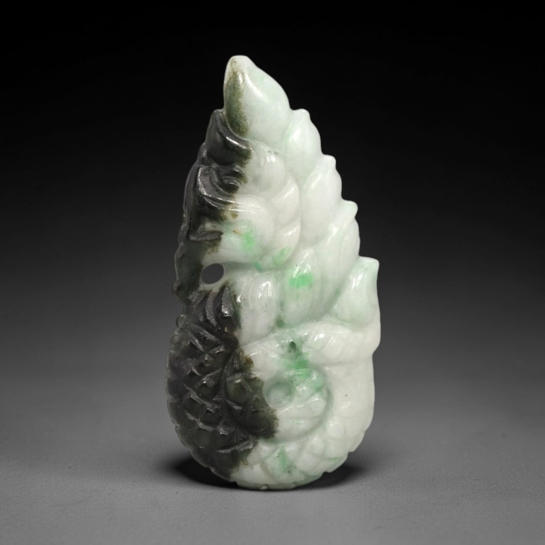 A Chinese Jadeite Jade Naga Pendant, 20th Century, 13FR: Carved from white and dark green jadeite jade with natural tonal variation and blackish mineral inclusions, the pendant features a naga form rendered in high relief. The naga's body is depicted with s