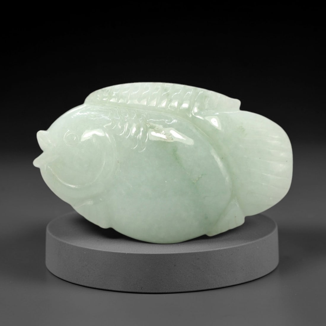 A Chinese Icy Jadeite Fish Pendant, 20th Century, 54FR: Carved from translucent icy jadeite with a pale greenish-white hue and minor natural inclusions, the pendant is shaped as a stylized fish with a rounded, plump body. Incised lines define the dorsal fi
