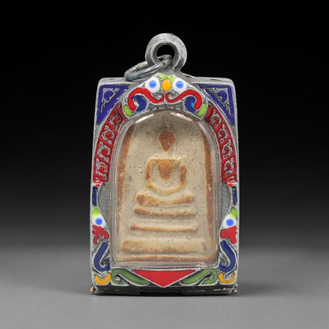 A Thai Terracotta Buddha Amulet in Metal Case, 20th Century, 76ZH: The amulet is formed from terracotta, with a light beige matrix containing visible particulate inclusions. The obverse depicts a seated Buddha in bhumisparsha mudra, seated on a multi-tiered base, enc
