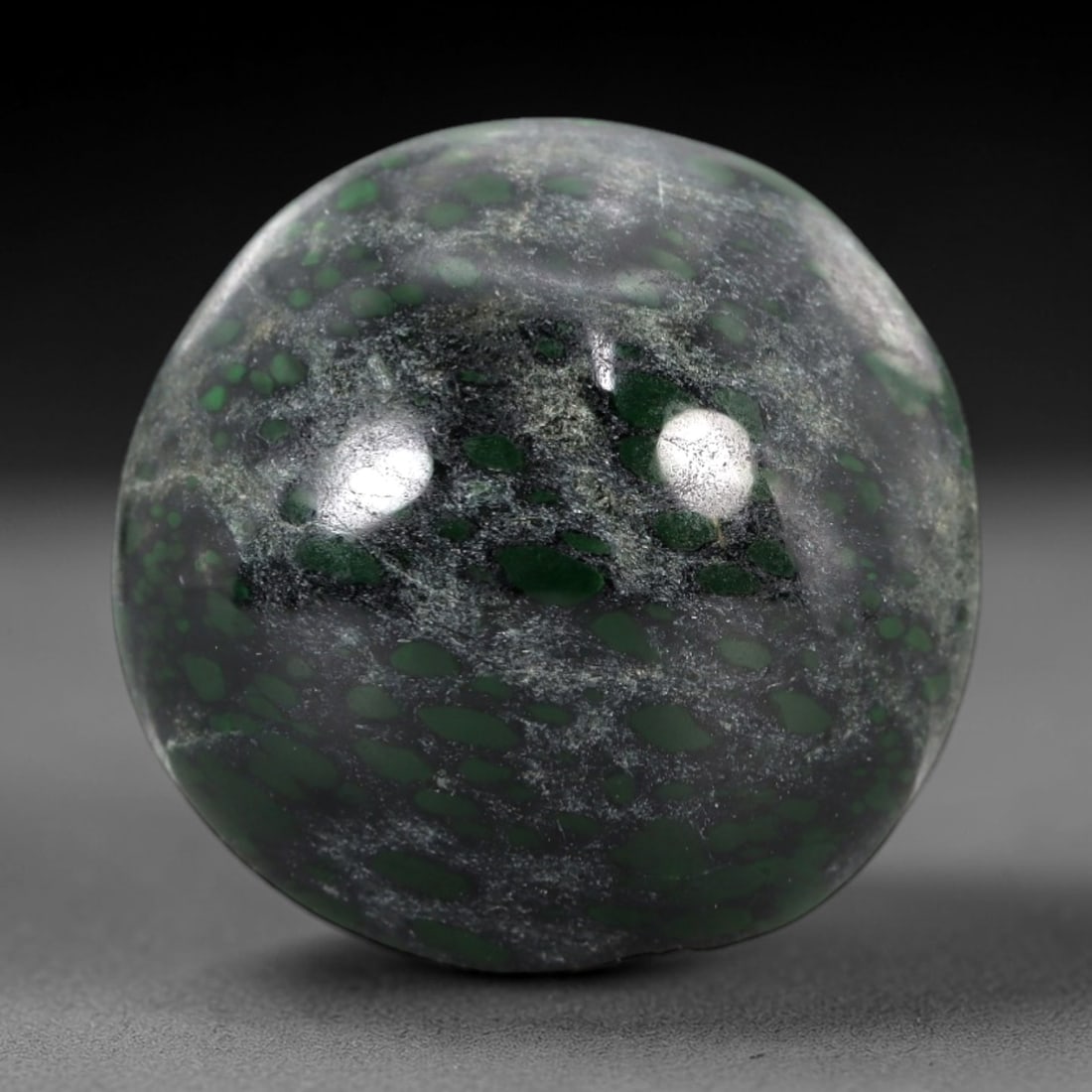 21.57 Carats Dark Matrix and Green Spot Maw Sit Sit Jade Cabochon - Natural Burmese Stone, 28AB: This maw sit sit jade cabochon is fashioned into an oval, domed form with a highly polished surface. The material exhibits a dark, semi-translucent to opaque matrix, densely interspersed with distinct