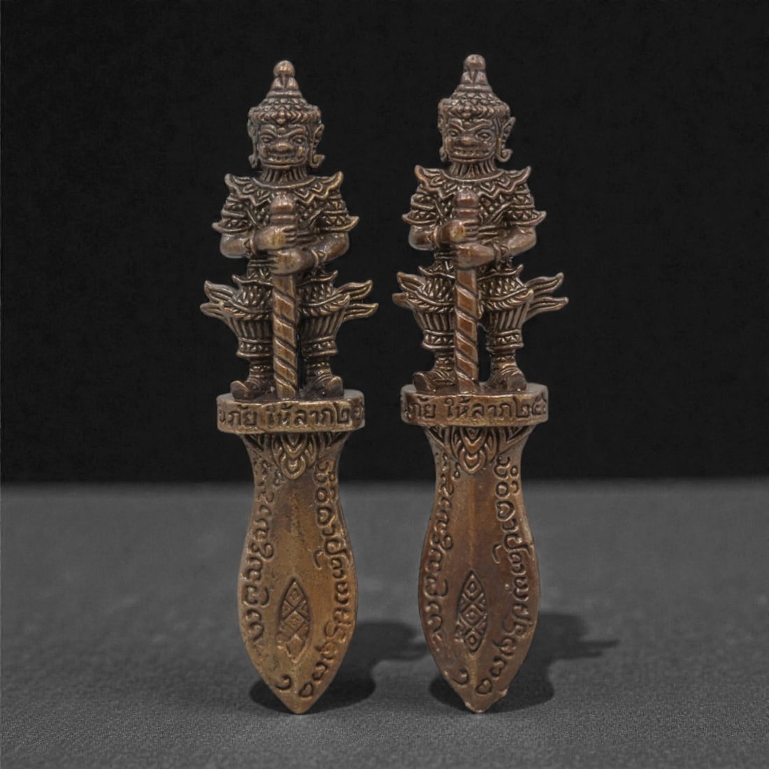A Pair of Thai Bronze Guardian Daggers, 20th Century, 14FM: Cast from bronze with a warm, aged patina, each dagger features a guardian figure (yaksha) standing atop a blade-shaped base. The figures are rendered in high relief, with fierce facial features, orna