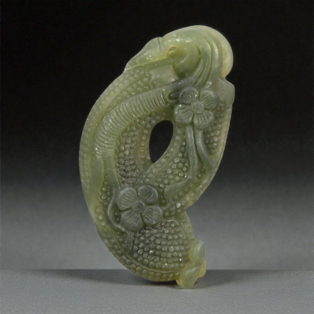 A Chinese Nephrite Jade Fruit Pendant, 20th Century, 77FA: Carved from greenish celadon nephrite jade with areas of darker tonal variation and soft translucency, the pendant is worked in the form of an elongated fruit with curling vine and floral motifs. The
