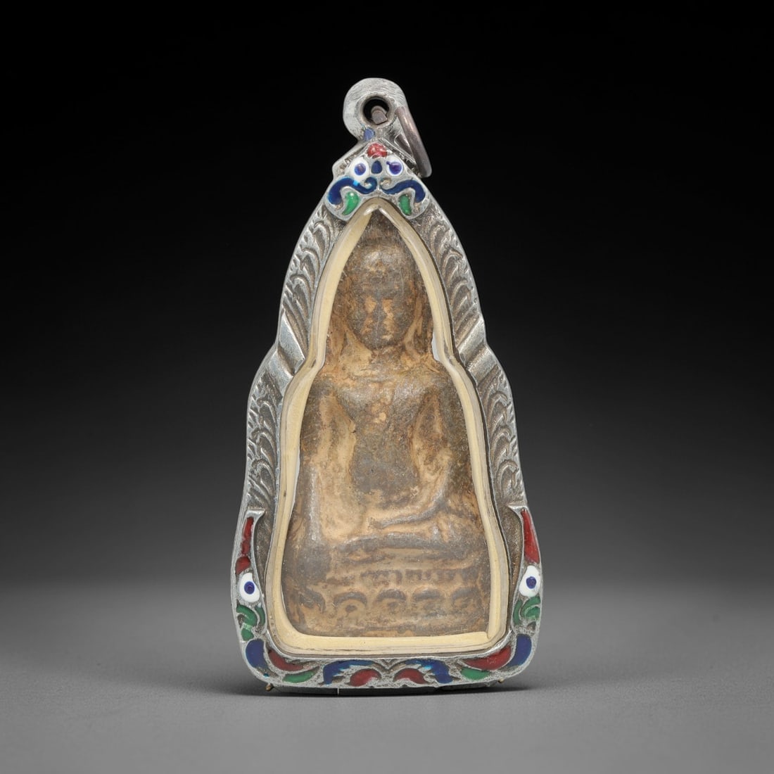 A Thai Buddha Amulet in Silver Enamel Case, Late 20th Century, 58ZH: A teardrop-shaped Buddha amulet, measuring 7.5 x 3.7 cm, housed in a hinged silver case with red, green, and blue enamel inlays. The obverse of the case displays a seated Buddha figure in relief, set
