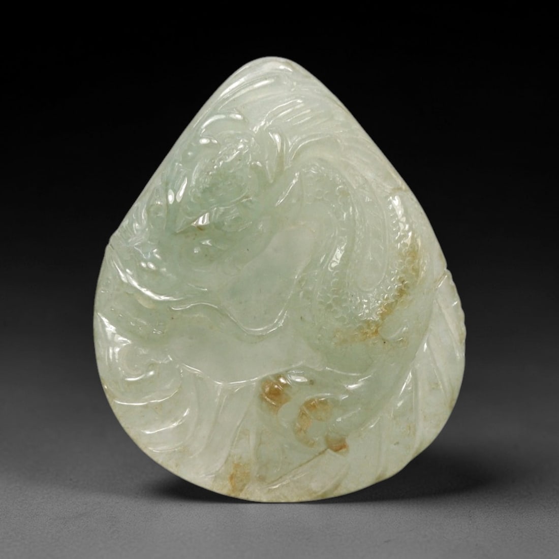 A Chinese Jadeite Jade Dragon Pendant, 20th Century, 21FR: Carved from pale green jadeite jade with natural tonal variation and scattered russet inclusions, the pendant is shaped as a teardrop form. A coiled dragon is rendered in low relief, with its head tur