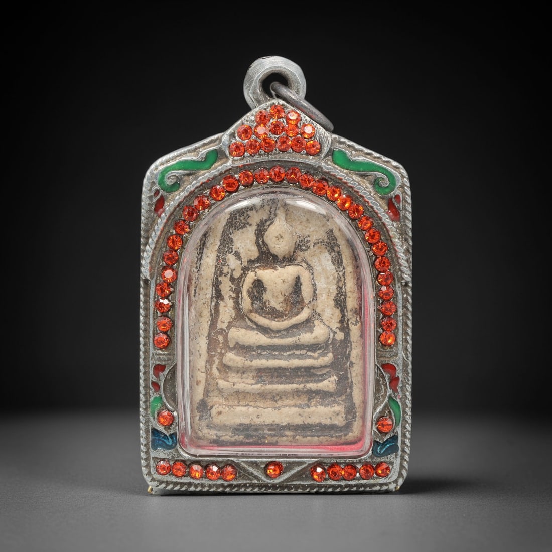 A Thai Terracotta Buddha Amulet in Metal Case, 20th Century, 81ZH: The amulet is formed from terracotta, with a light beige matrix containing visible particulate inclusions and surface discoloration. The obverse depicts a seated Buddha in meditative posture, seated o