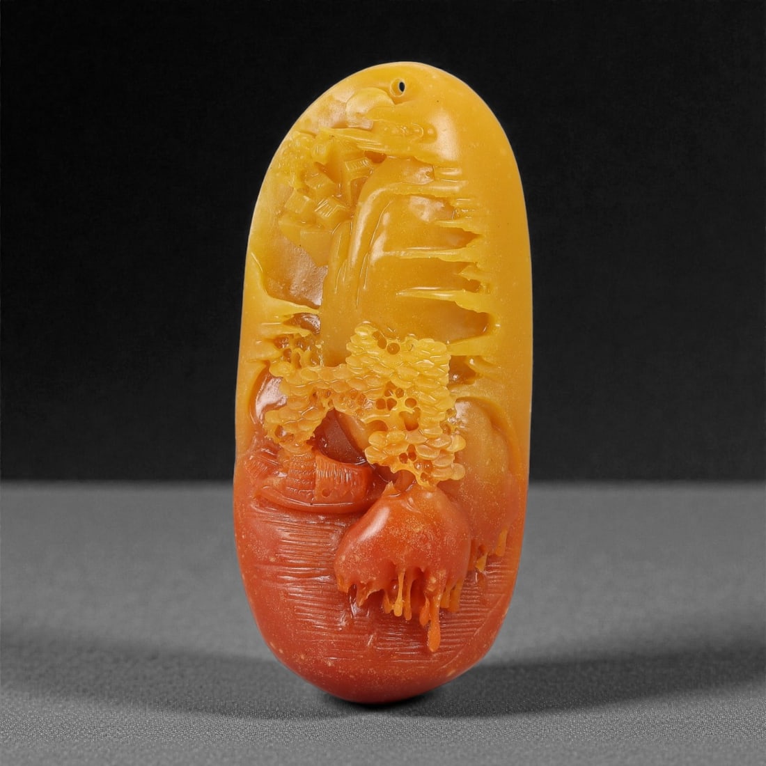 A Chinese Hardstone Carved Pendant, 20th Century, 48FD: Carved from a translucent hardstone with natural color gradation ranging from honey yellow to deep orange-red. The pendant is vertically oriented with an elongated oval profile and a rounded top, pier