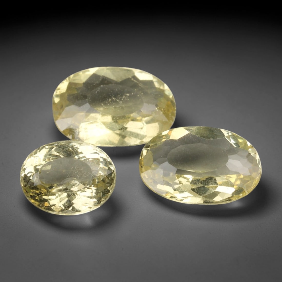 4.58 Carats Pale Yellow Apatite Parcel - Natural Loose Gemstones, 3XP: This luminous parcel of three oval-cut apatite gemstones, weighing a total of 4.58 carats with individual dimensions ranging from 7.4 to 9.9 mm, radiates a soft, buttery pale yellow hue. The faceted c