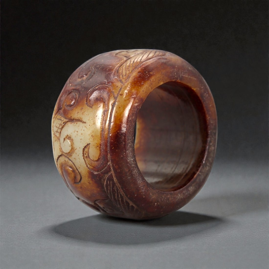 A Chinese Nephrite Jade Ring, 20th Century, 13FA: Carved from mottled brown and pale celadon nephrite jade with natural color variation and areas of translucency, the ring is formed with a thick circular profile and a wide band. The exterior surface