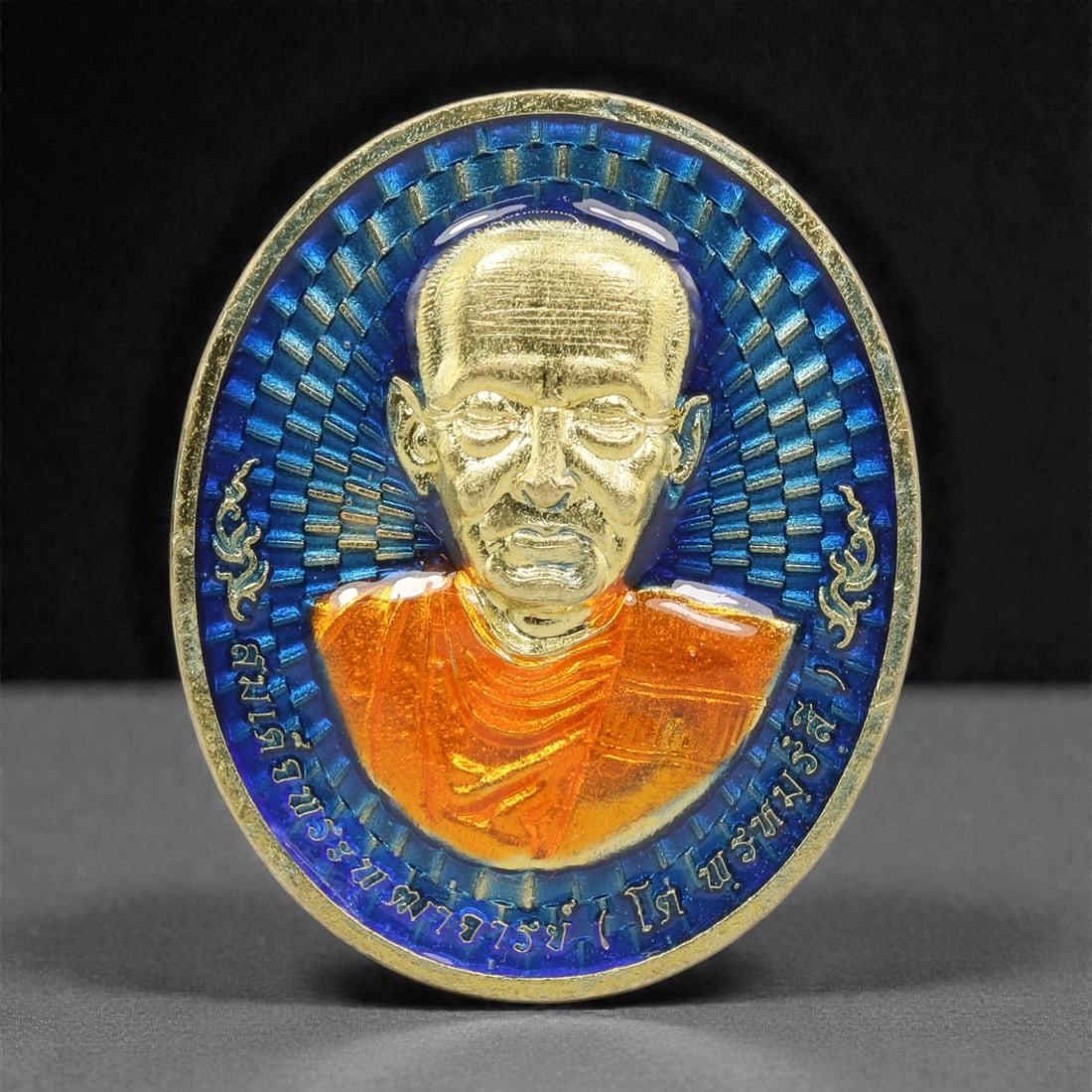 A Thai Gilt-Metal and Enamel Monk Portrait Medallion, 21st Century, 87FP: Cast from metal with a gilt surface finish, the medallion is oval and double-sided with a raised gilt-metal border. The obverse features a high-relief gilt bust portrait of a Buddhist monk, set agains